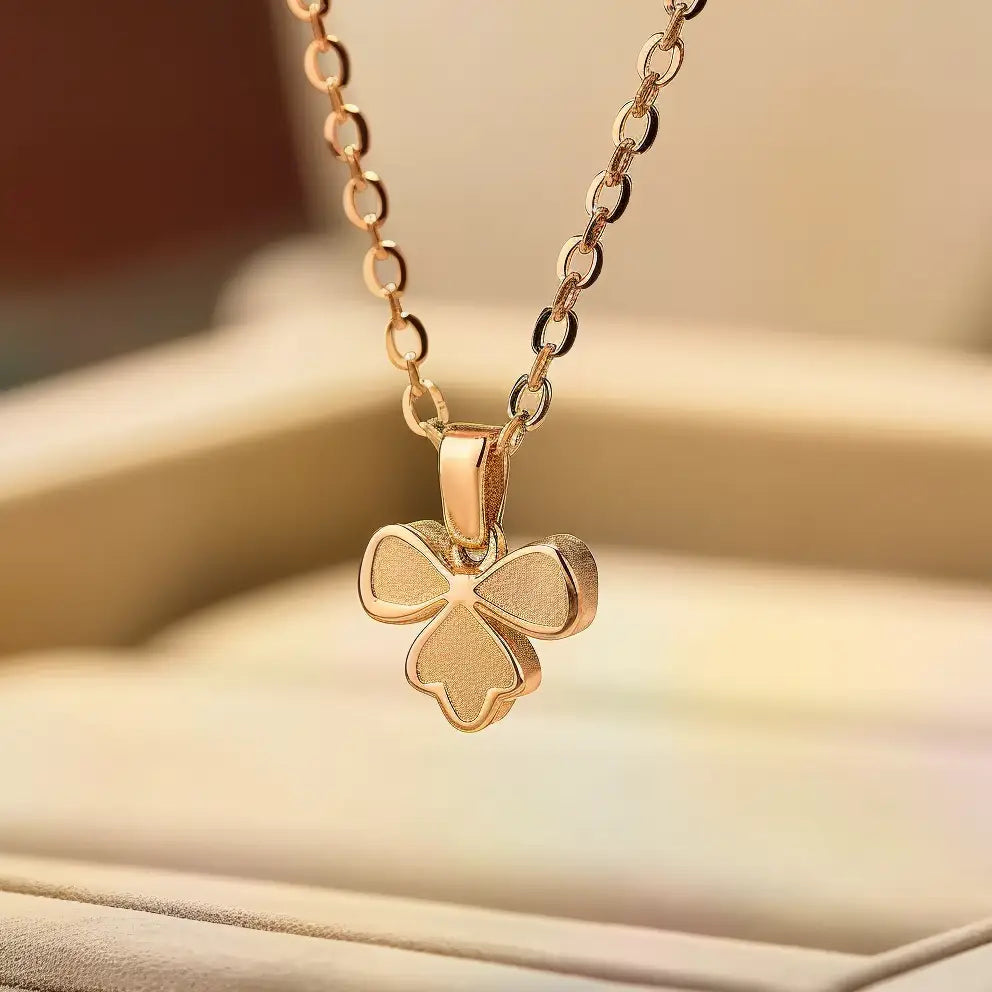 A gold pendant necklace featuring a delicate four-leaf clover design, displayed against a soft, blurred background.