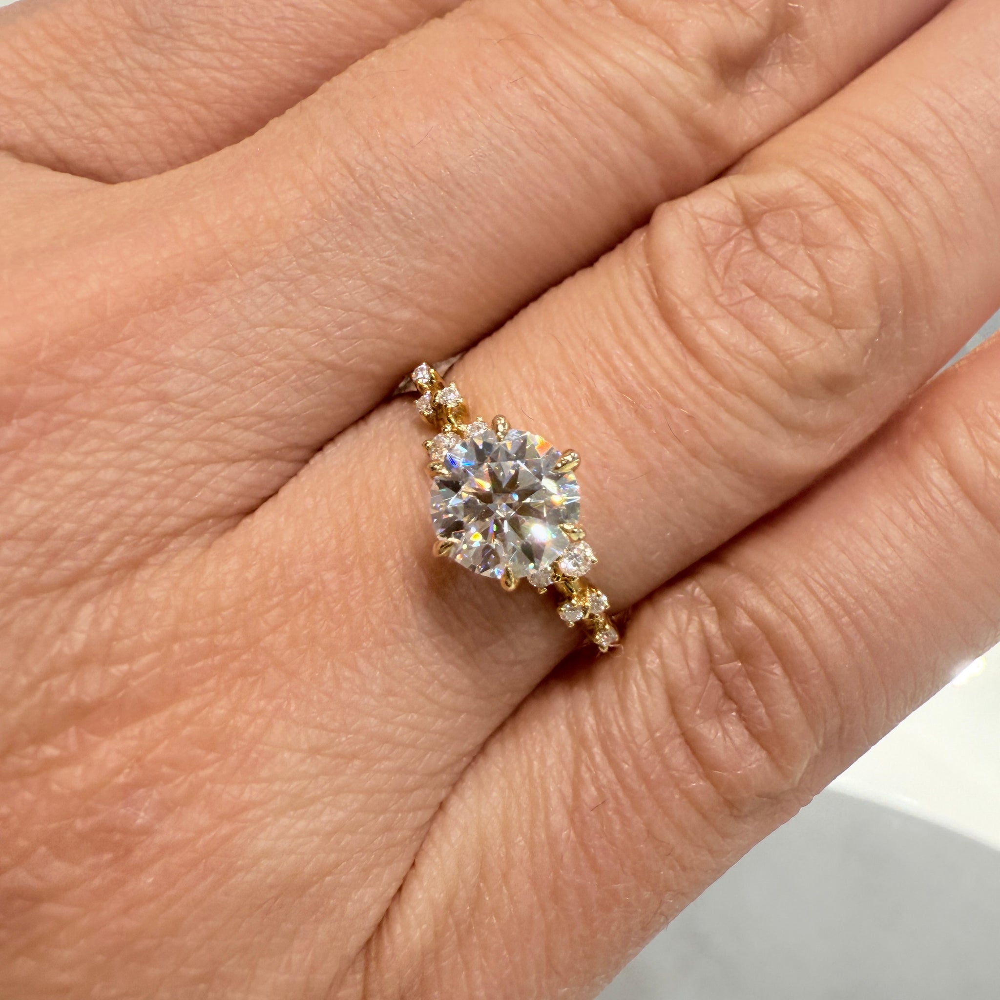 1 Ct round moissanite engagement ring with accent stones in 14K gold.