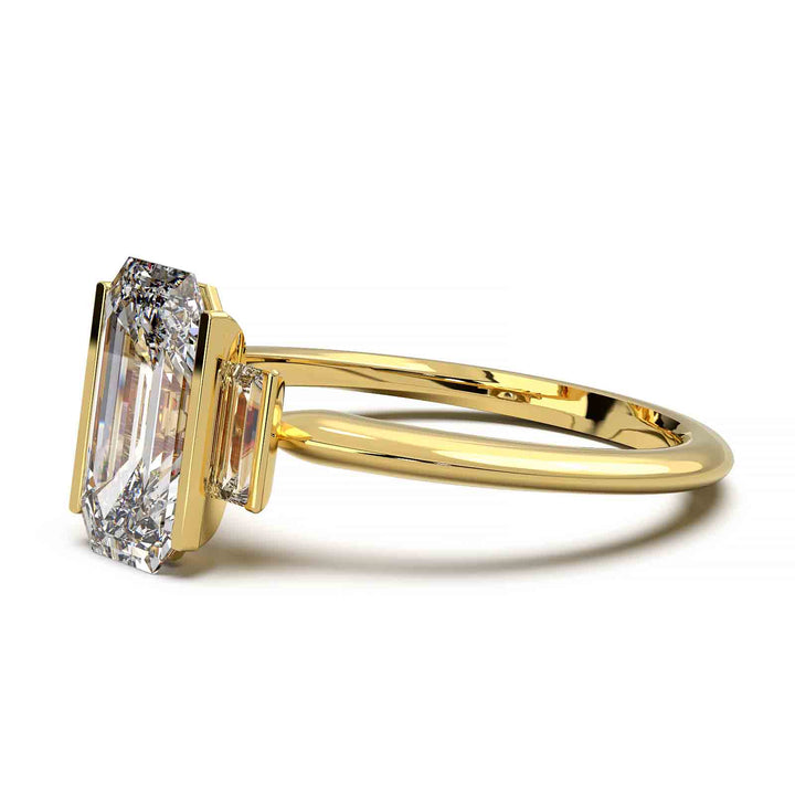 Three-stone engagement ring with emerald-cut diamond, baguette side stones, and modern bar prong setting.
