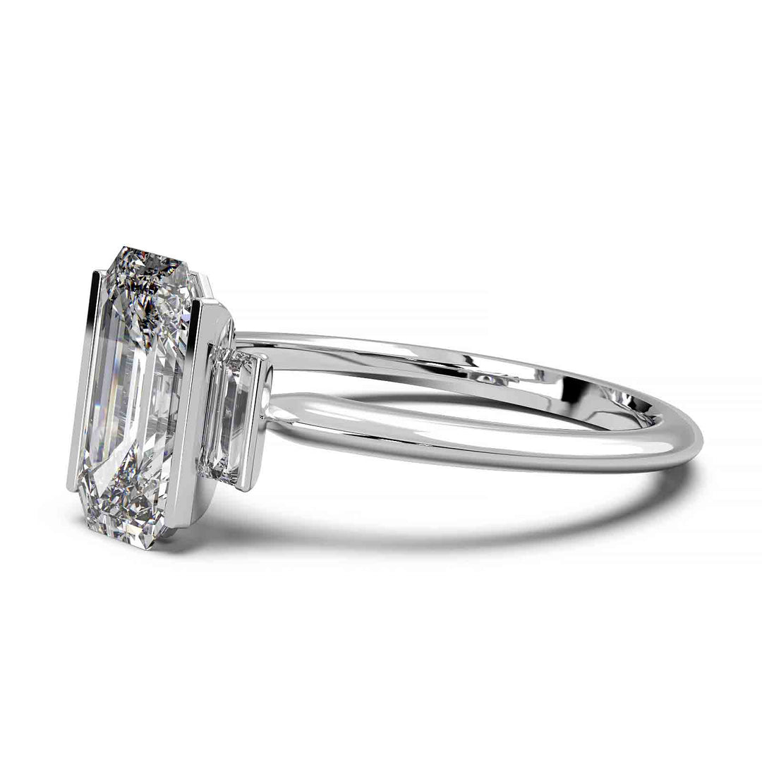 Three-stone engagement ring with emerald-cut diamond, baguette side stones, and modern bar prong setting.