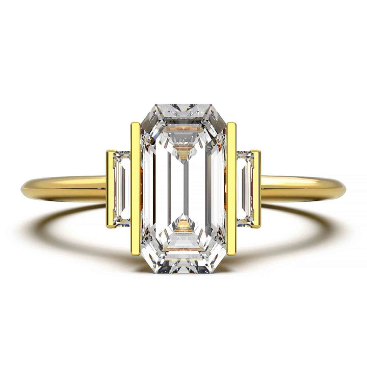 Three-stone engagement ring with emerald-cut diamond, baguette side stones, and modern bar prong setting.