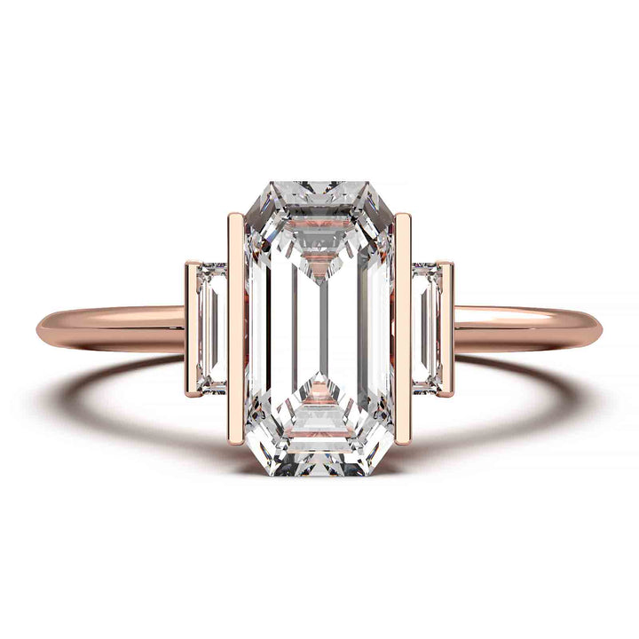 Three-stone engagement ring with emerald-cut diamond, baguette side stones, and modern bar prong setting.