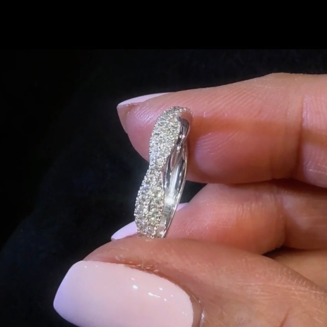 twisted style diamond wedding band held between fingers against a dark background