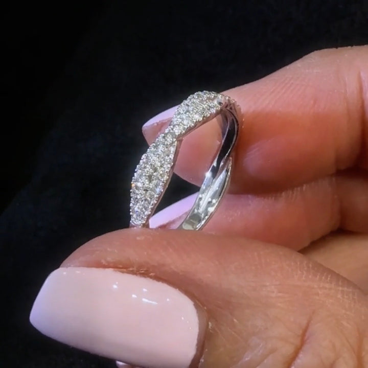 twisted style diamond wedding band held between fingers against a dark background