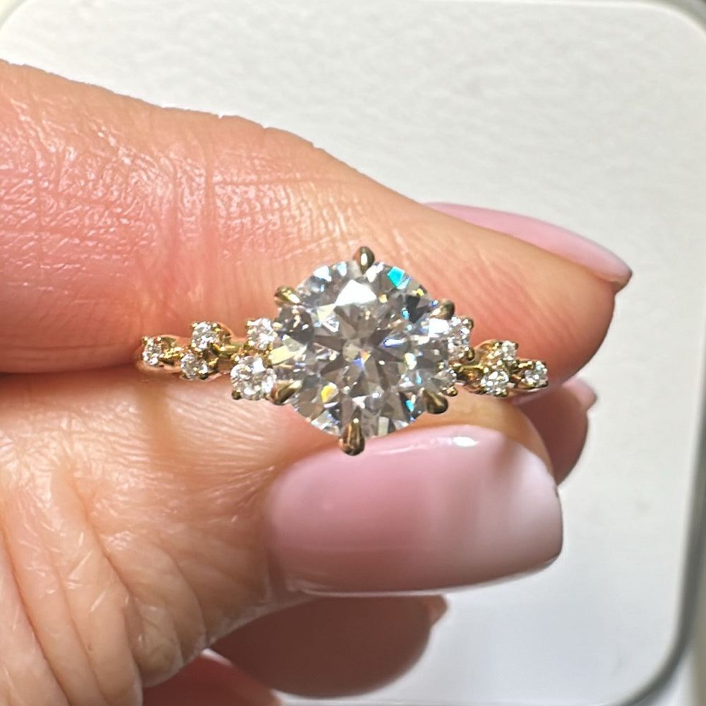 1 Ct round moissanite engagement ring with accent stones in 14K gold.